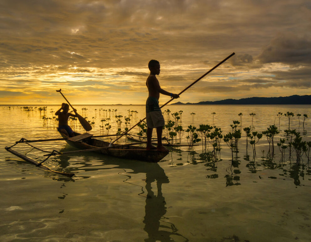Sunset silhouette of a local paddling a traditional canoe across calm waters.