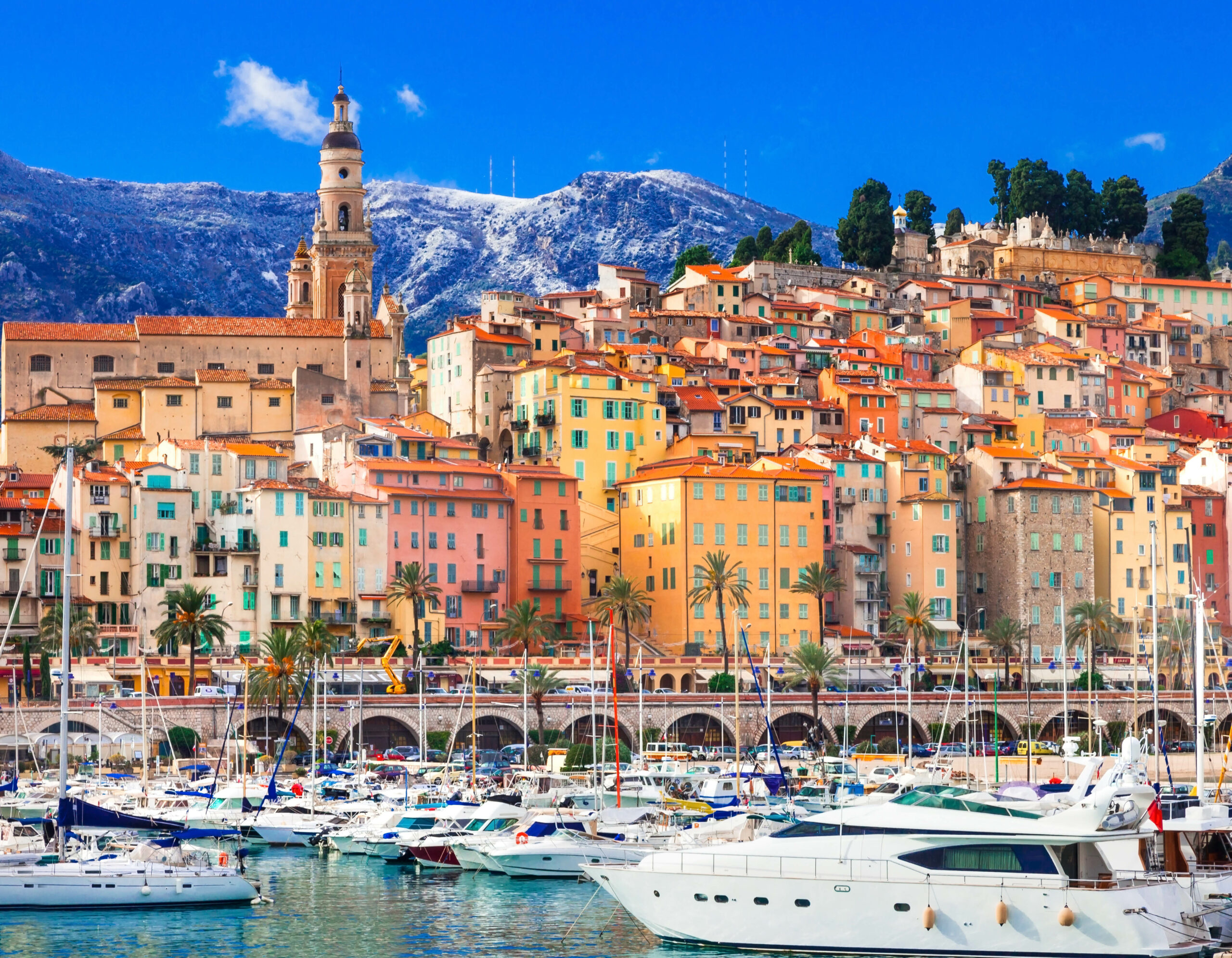 Port of Menton, featuring an array of luxury yachts and sailing boats. In the background, the colorful old town, nestled the majestic mountains.