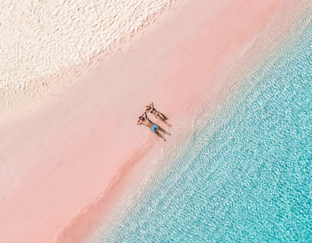 Pink Beach in Komodo with two tourists sunbathing, drone view