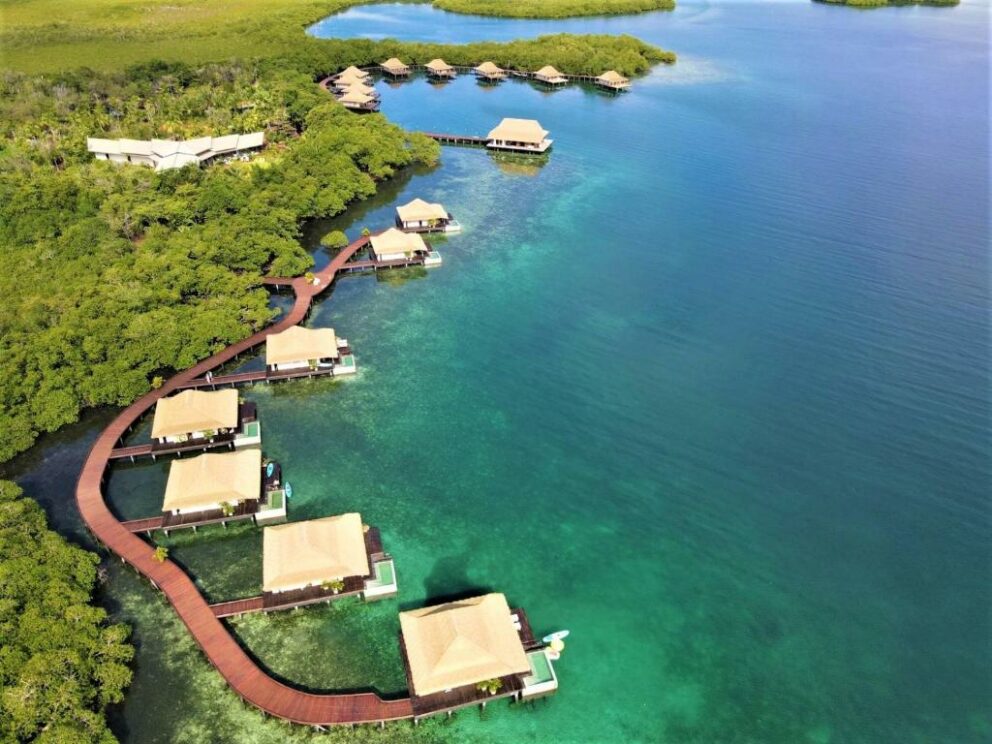 Aerial view of overwater bungalows surrounded by mangroves and turquoise water in Bocas del Toro, Panama, connected by a wooden boardwalk.