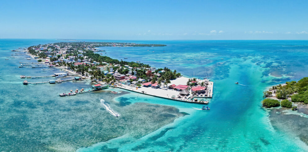Aerial view of Caye Caulker, Belize, with turquoise waters, sandy beaches, docks, and colorful buildings surrounded by coral reefs in the Caribbean Sea.