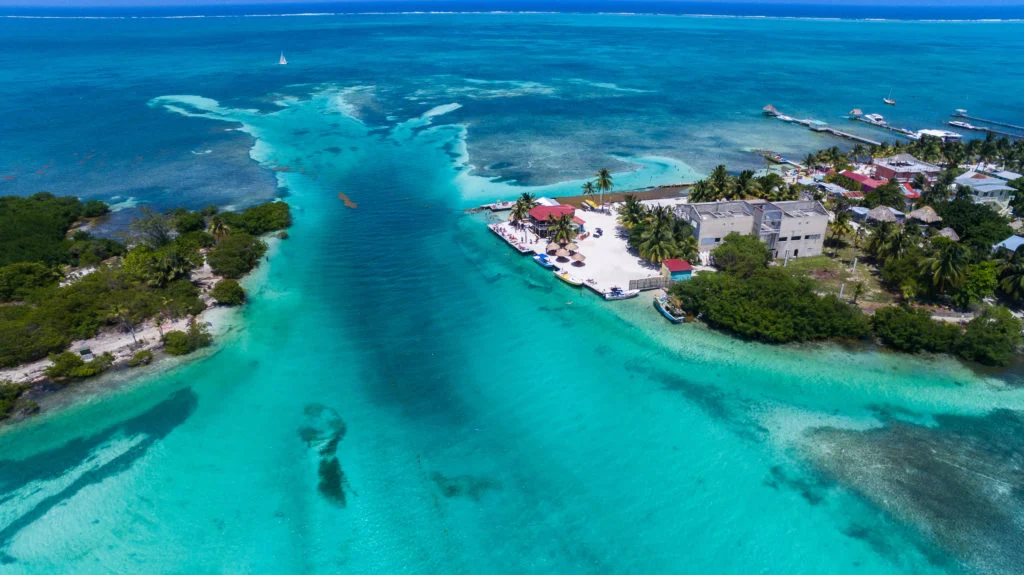 Aerial view of The Split in Caye Caulker, Belize, showing turquoise waters, sandy shores, palm trees, and small beachside bars along the channel.