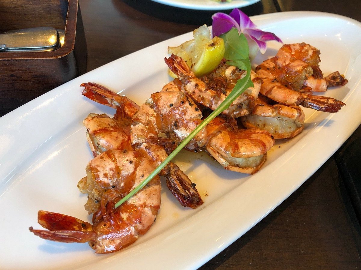 Grilled shrimp dish garnished with lemon and an orchid on a white plate