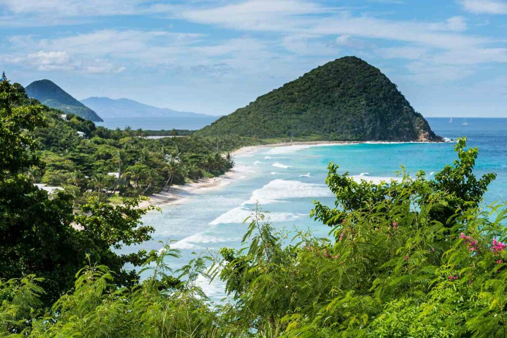 Panoramic view of Long Bay Beach in Tortola, British Virgin Islands, featuring a long sandy beach, turquoise ocean waves, and lush green hillsides.