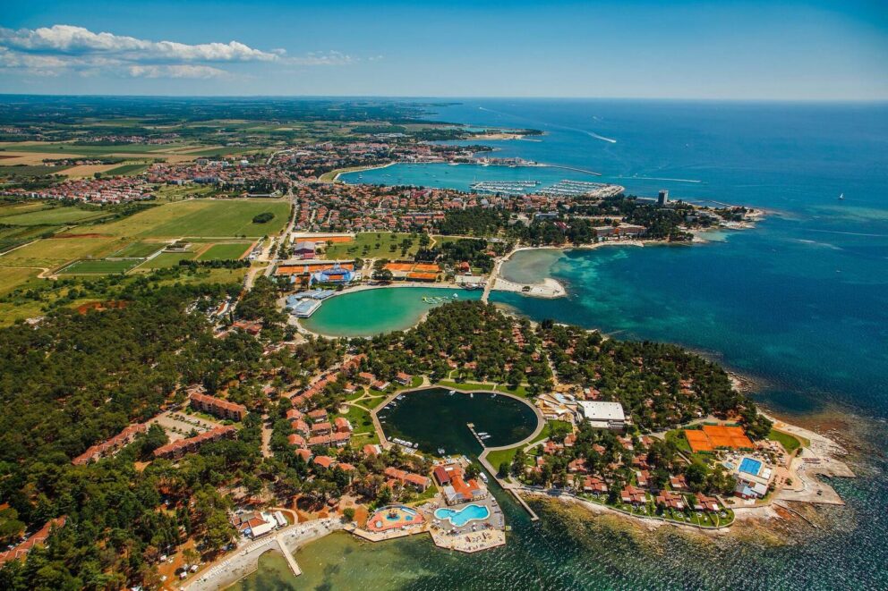 aerial view of the Stella Maris Resort in Umag, Croatia, showing the coastal landscape with the resort's buildings, swimming pools, tennis courts, and a marina surrounded by lush greenery and the Adriatic Sea