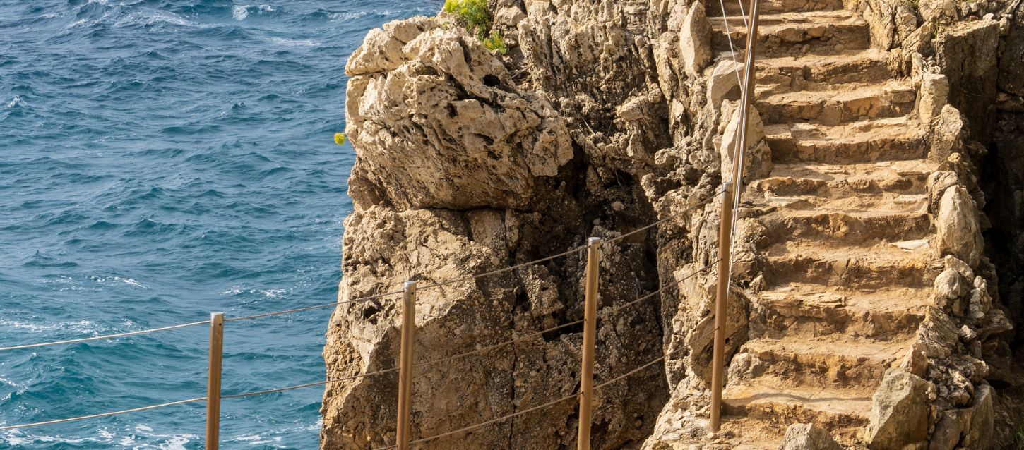 Rocky smuggler’s trail winding along the coastline, with uneven stone steps and rugged cliffs