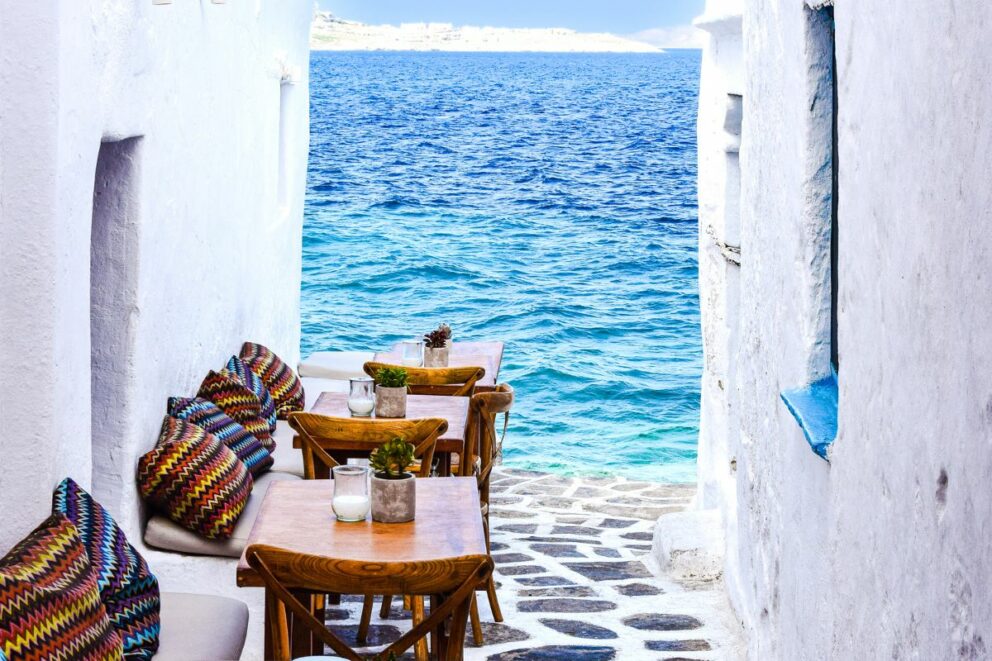 A picturesque village with traditional white buildings is perched on a rocky hill overlooking the sea under a dramatic blue sky with clouds. The village is located on the Greek island of Sikinos.