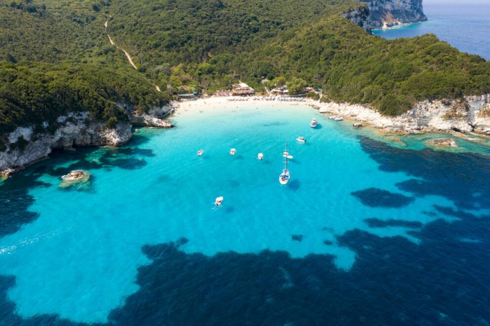 Small cove in Paxos with a beach bar and boats anchored in turquoise water