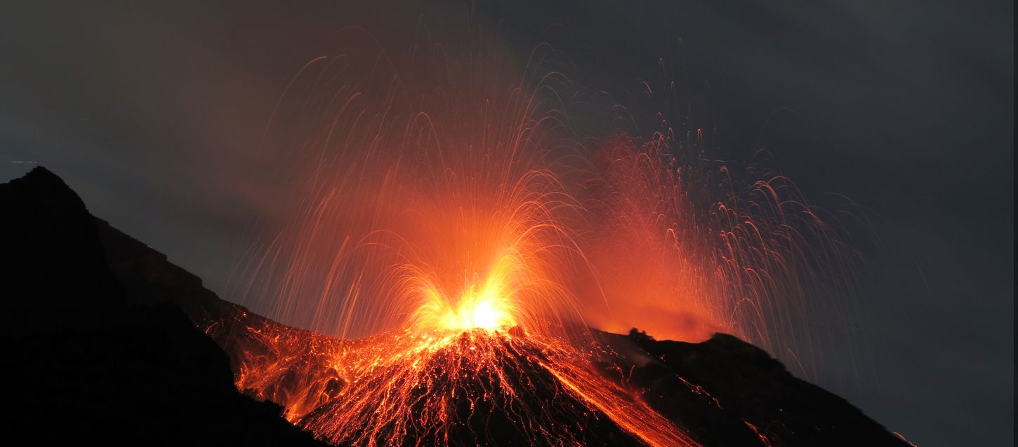 volcanic eruption at night, with molten lava and glowing rocks spewing from the crater