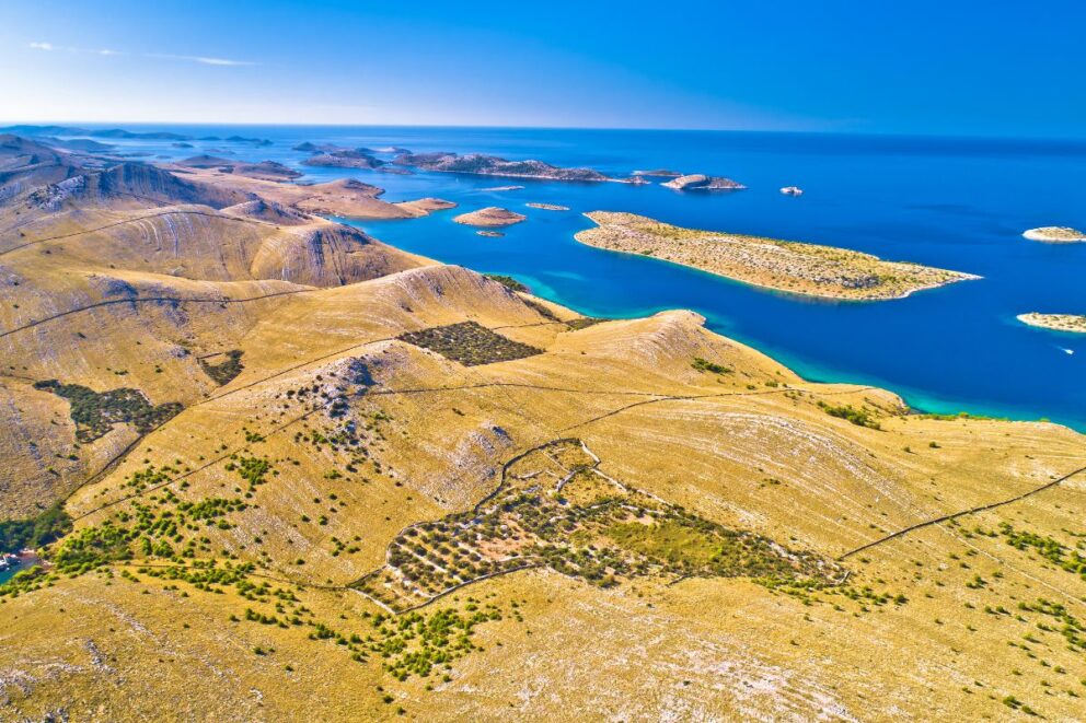 Aerial view of Kornati Islands National Park in Croatia, showing rugged golden hills, scattered small islands, and deep blue Adriatic waters under a clear sky.