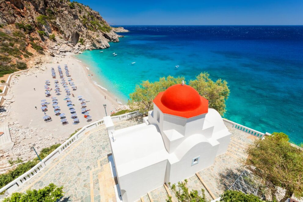 The image displays the picturesque Kyra Panagia beach, a small seaside resort on the island of Karpathos, Greece.