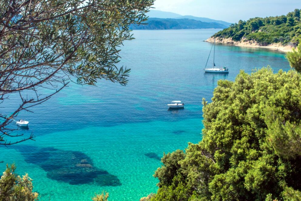 The image depicts a beautiful turquoise sea and coastline on the Greek island of Skiathos.