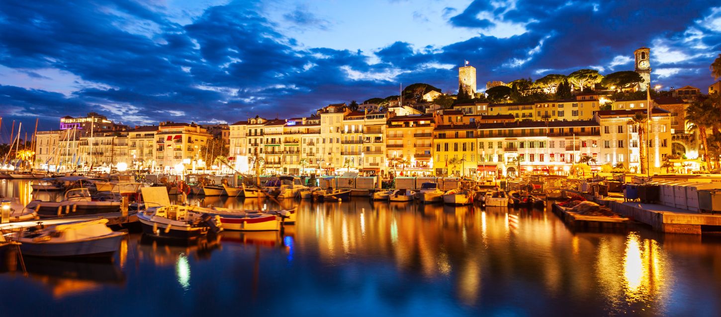 Port with moored boats and the old town of Cannes illuminated at night