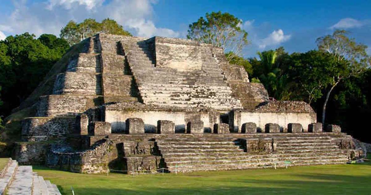 Ancient Mayan pyramid ruins of Altun Ha near Belize City, surrounded by lush green trees under a blue sky with scattered clouds.