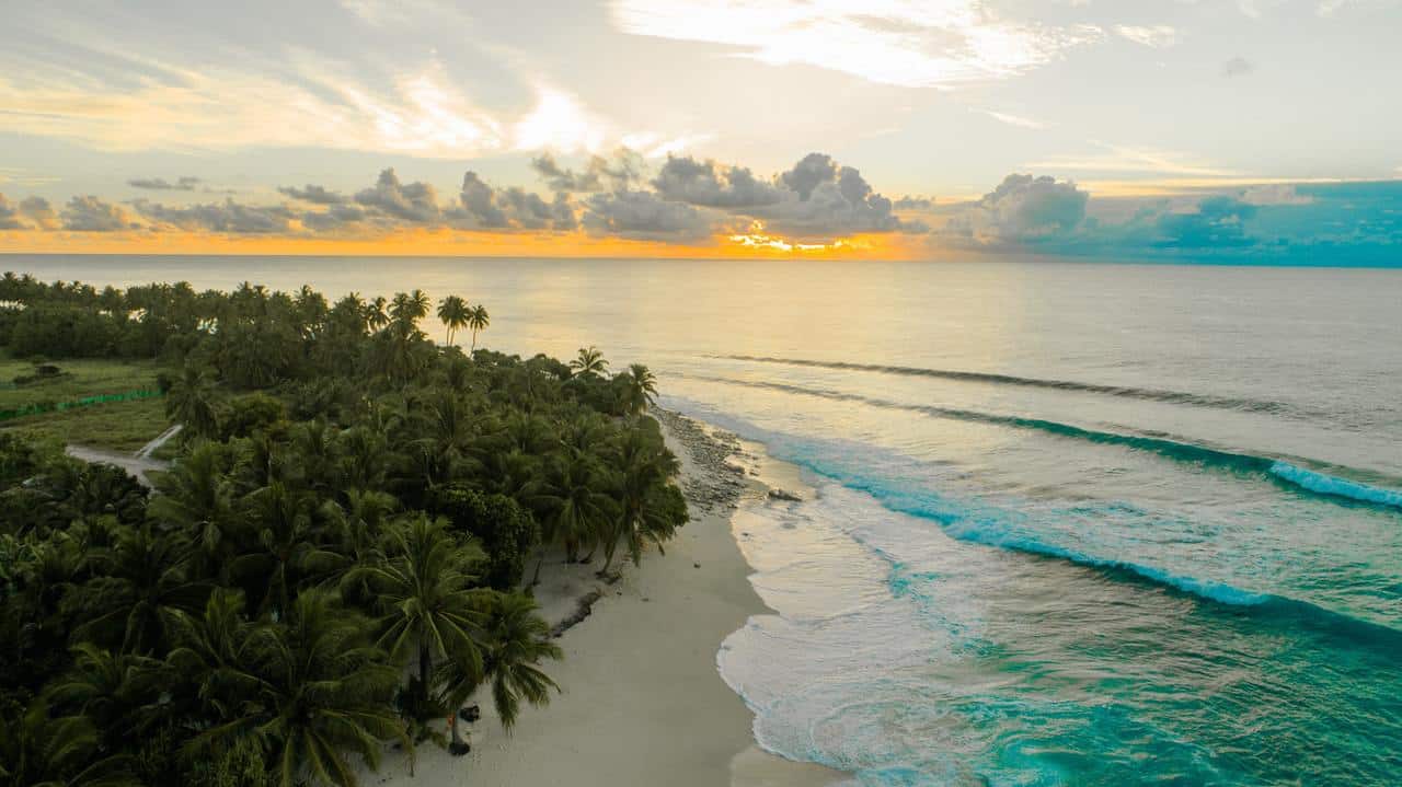 Aerial view of Secret Beach in Ambergris Caye, Belize, at sunset with palm trees, gentle waves, and a golden sky over the Caribbean Sea.