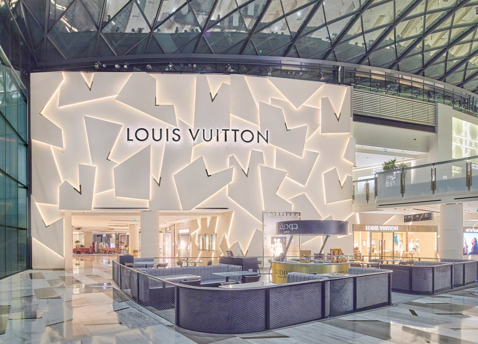 Interior view of The Galleria mall in Abu Dhabi featuring the Louis Vuitton store with a striking geometric illuminated wall design, marble floors, and modern architecture under a glass-domed ceiling.