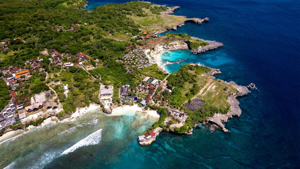 Aerial view of Nusa Lembongan, Bali, showing turquoise lagoons, rocky cliffs, and small beaches surrounded by lush greenery and coastal villages with scattered resorts.