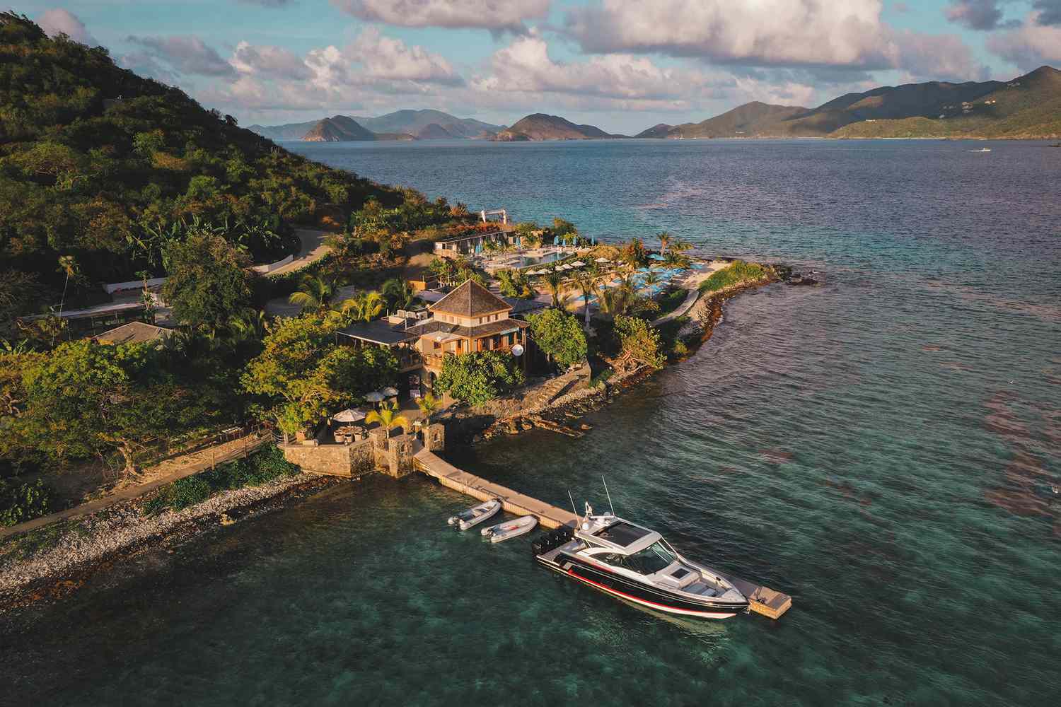 An aerial view of the Lovango Resort & Beach Club, showing resort buildings with a dock extending into turquoise water where a large boat is moored