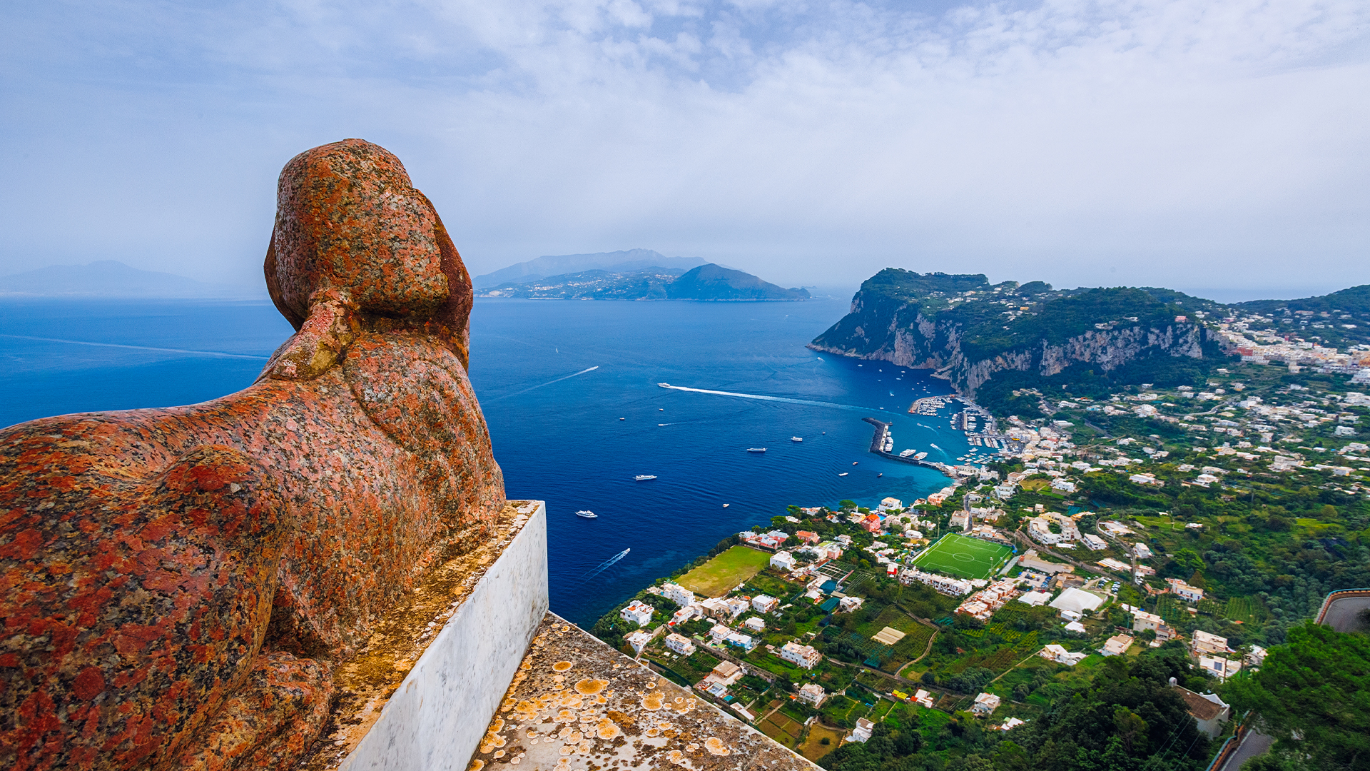 Capri with coastal houses, blue sea and yachts cruising nearby